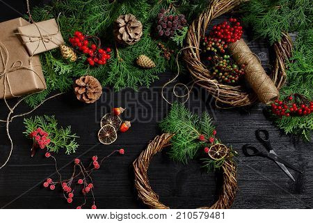 Make a Christmas wreath with your own hands. Spruce branch, Christmas wreath and gifts on a black wooden background. Workplace for preparing handmade decorations.