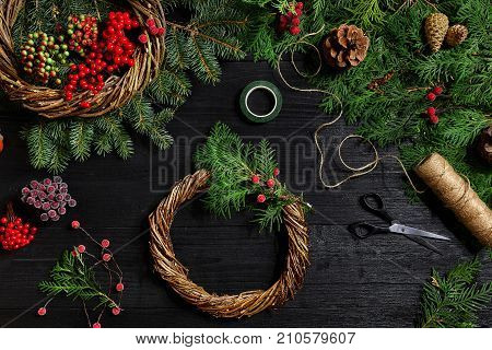 Make a Christmas wreath with your own hands. Spruce branch, Christmas wreath and gifts on a black wooden background. Workplace for preparing handmade decorations.
