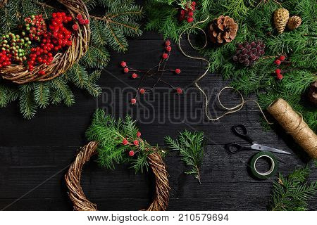 Make a Christmas wreath with your own hands. Spruce branch, Christmas wreath and gifts on a black wooden background. Workplace for preparing handmade decorations.