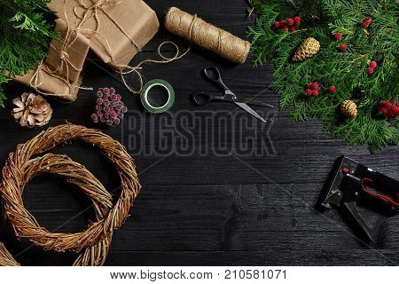 Make a Christmas wreath with your own hands. Spruce branch, Christmas wreath and gifts on a black wooden background. Workplace for preparing handmade decorations.