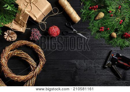 Make a Christmas wreath with your own hands. Spruce branch, Christmas wreath and gifts on a black wooden background. Workplace for preparing handmade decorations.