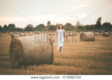 Beautiful Girl Running In The Field With A Bales Of Hay