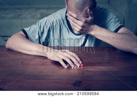 Depressed man suffering from suicidal depression want to commit suicide by taking strong medicament drugs and pills and he is cover his face with his hand