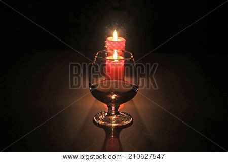 A glass of cognac or whiskey and candle on black background. christmas composition
