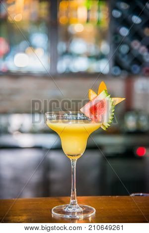 Cocktail drink in yellow favor with piece of watermelon and orange on top on wooden cocktail bar
