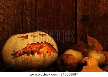 Halloween pumpkin and apples on autumn leaves next to a wooden background