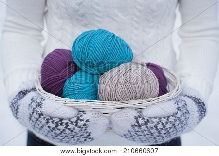 Wool yarn in a white basket. White and brown knitted wol-ol mittens. White knitted sweater background. Winter view. Snowy.