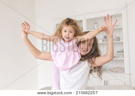 Little girl with her mother playing in flight airplane. You are my little bird Cheerful beautiful young woman holding baby girl in her hands and looking at camera at home
