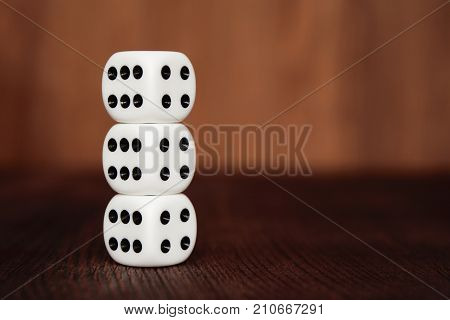 Three white plastic dices on each other on brown wooden board background. Six sides cube with black dots. Number 4 and 6.