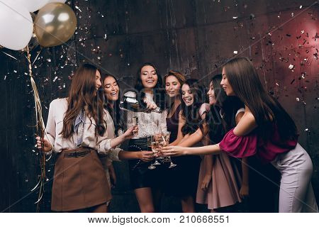 Beautiful girls celebrate New Year. Enjoying carefree time together. Group of beautiful young girl throwing gold confetti and looking happy and drinking champagne