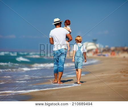 rear view of family father with kids walking on sandy beach near the sea summer vacation