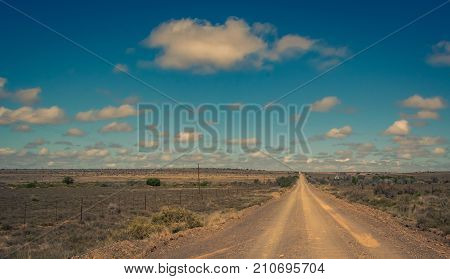 A dry dusty dirt road leads straight to the horizon in the arid Karoo area of South Africa