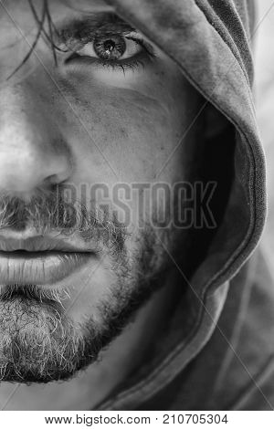 Bearded man young handsome guy male with beard and half face grey eye in hood on head outdoors