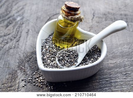 Chia oil with chia seeds in white heart shaped bowl on old wooden background.Organic chia seeds and oil.Healthy food,superfood or bodycare concept.Selective focus.