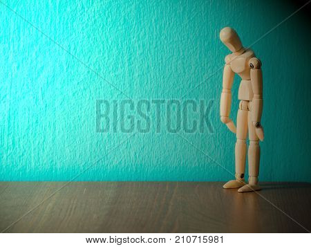 Sad wooden puppet are exhausted and hopeless.Wooden puppet stand on the wooden table. the background is turquoise and copy space for content.