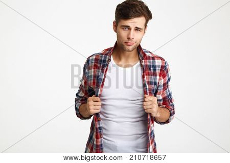 Close-up portrait of playful young macho holding hes checkered shirt, looking at camera, isolated on white background