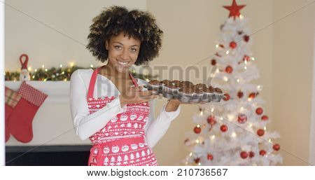 Smiling happy woman in a festive red apron standing in front of the Christmas tree with tray of freshly baked muffins