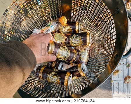 STRASBOURG FRANCE - SEP 24 2017: POV Male hand throwing taking Grimbergen beer aluminium can in a public waste bin - homeles concept
