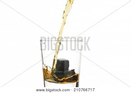 Whiskey pours into a glass with stones.