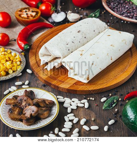 Vegetarian burrito on wooden board over black table surrounded by ingredients