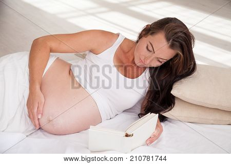 A Pregnant Woman Lies On A Bed And Reading A Book 1
