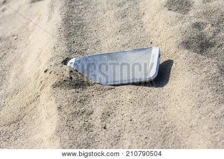 Lost white smartphone with crack on the screen lying in the sand