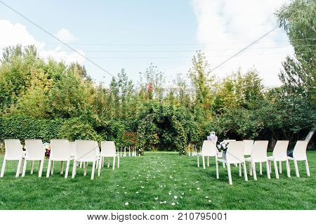 Place for wedding ceremony with white chairs and an arch of living plants