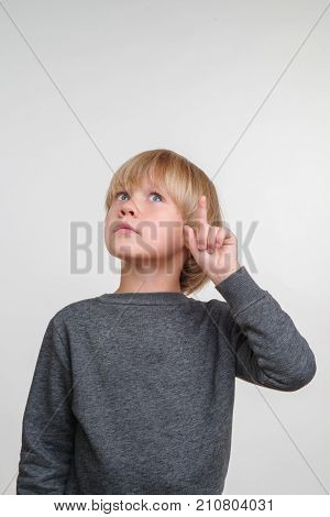 Funny little boy in a gray pullower posing on the camera in studio. Pensive child on the gray background. Close-up of little boy.