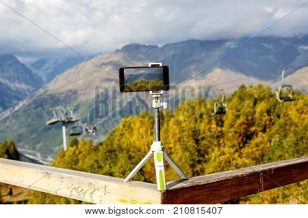 smartphone on a tripod in the mountains, a lift and a rainbow on the background
