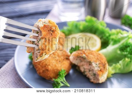 Fork with piece of salmon patty over plate, closeup