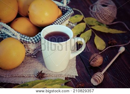 tea with lemon, honey, oranges, autumn leaves on woodenbackground