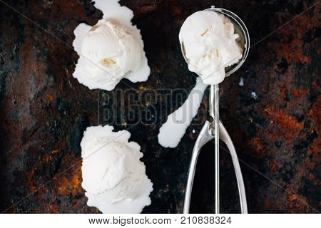 Top view of ice cream scooper with balls of ice cream on black rustic background