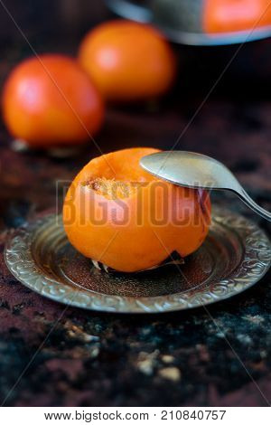 Someon start to eat persimmon on siver plate over rustic surface