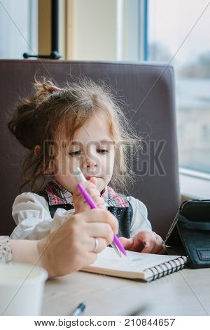 Little kid girl writing or drawing with pen in scetch book.