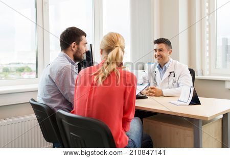 family planning, medicine, fertility and healthcare concept - couple visiting doctor and filling form at clinic