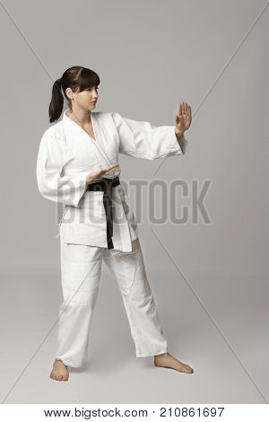 Young woman practicing karate on light background