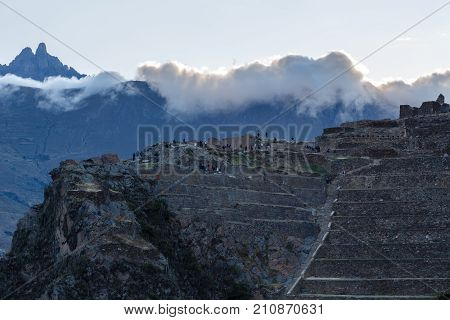 People Walking On The Terraces Of Pumatallis, Ancient Inca Fortress And Mountains Covered In Clouds,