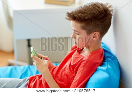 childhood, cyberbullying and communication concept - boy with smartphone lying on bed at home