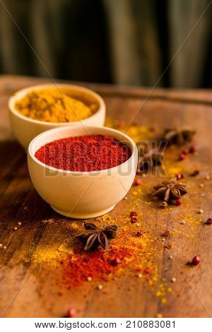 Close up two bowls filled with red paprika and yellow turmeric powder on dark wooden table covered with anise