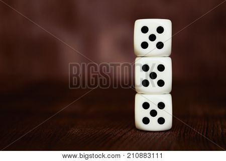Three white plastic dices pile on dark brown wooden board background. Six sides cube with black dots. Lucky number 555.