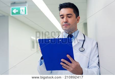 medicine, healthcare and people concept - doctor writing to clipboard at hospital