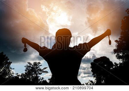 Blurred of silhouette businesswoman hands raised and holding gold medals with ribbon against sunset background to show team success in business Winners success award concept.