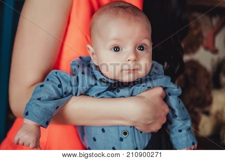 Portrait of newborn baby on mothers hands. Wearing blue shirt, tie bow and trousers. Lifestyle horizontal close up photo.
