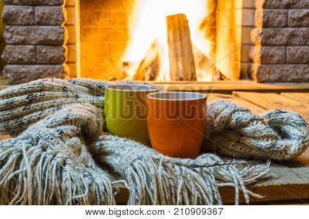 Two mugs for tea or coffee woolen things near cozy fireplace in country house winter vacation horizontal.