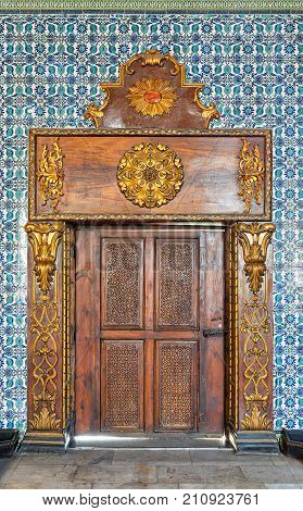 Cairo, Egypt - October 21, 2017: Closed wooden engraved aged door framed by golden ornate wooden frame on Turkish ceramic tiles wall with floral blue patterns Mosque of Manial Palace of Prince Mohammed Ali Tewfik Cairo Egypt