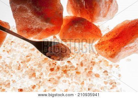 Pink Himalayan rock salt crystals with mineral spice serving spoon against illuminated white background. Healthy diet therapeutic food ingredient supplement.