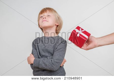 Little blond emotional boy in a festive red hat in a gray jacket. Little Santa Claus on a gray background.