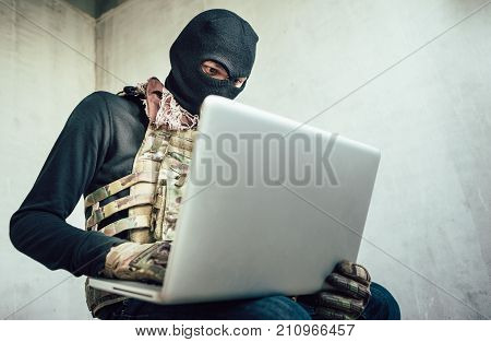 Terrorist is using a computer to perform a security drill fighter from an abandoned house.