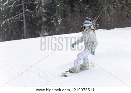 Young woman snowboarder in motion on snowboard in mountains.