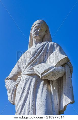 Statue of Poet Dante Alighieri with blue sky in the background. The writer has a book in his hand.
